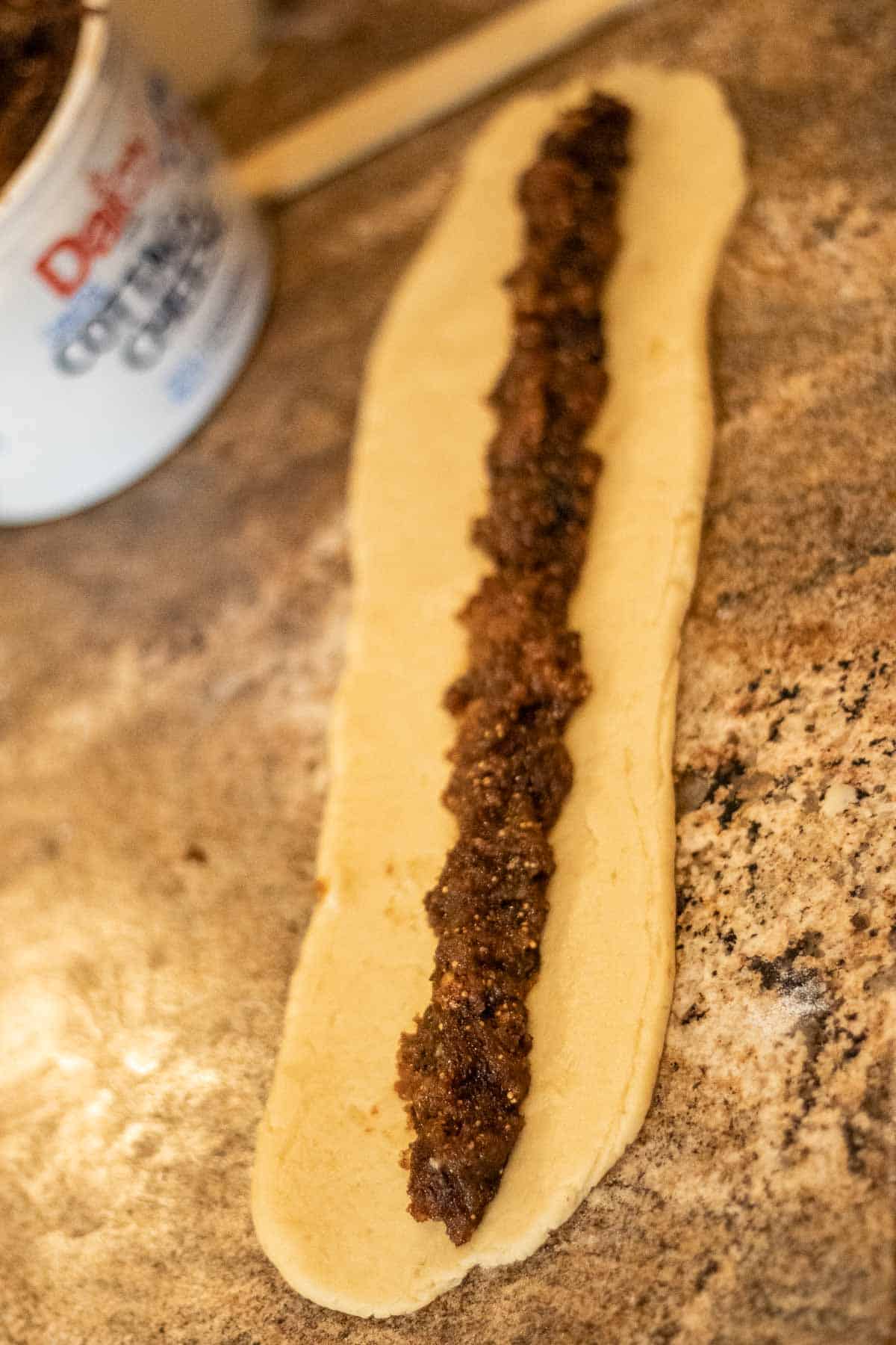 A strip of cookie dough with fig filling placed in a line down the center.