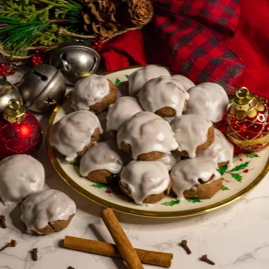 A christmas scene with a plate of Italian chocolate spice cookie with white glaze frosting.
