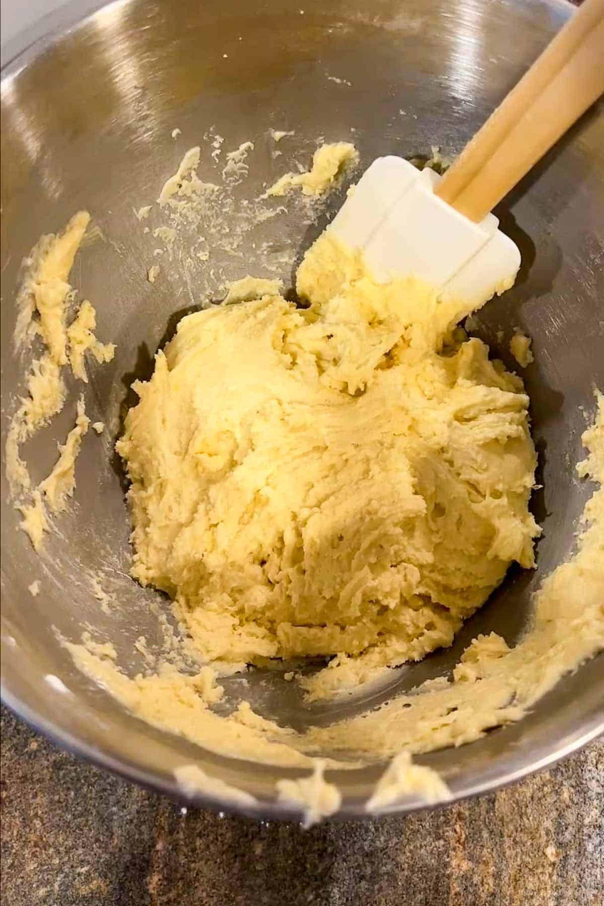 Cookie dough and a spatula in the bowl of a stand mixer.  