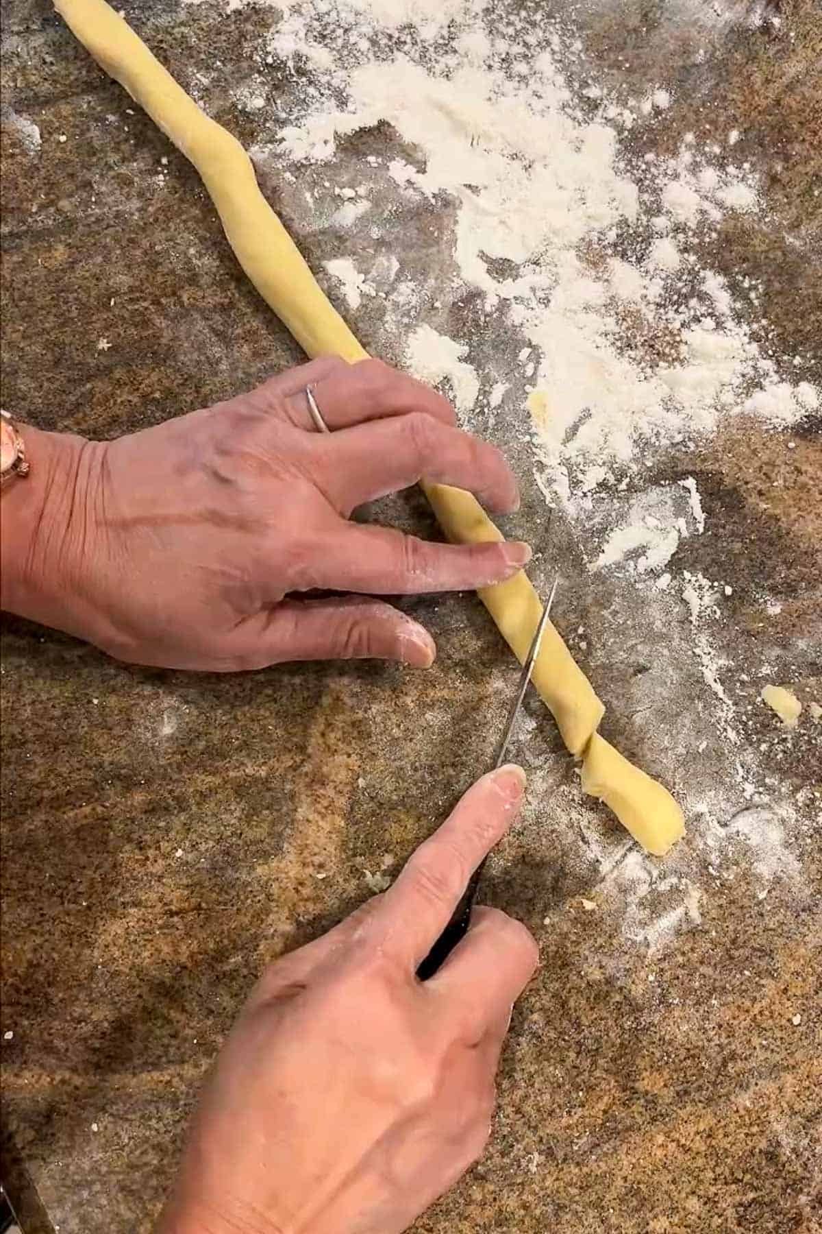 Cookie dough log that is being cut on an angle into individual cookie logs.