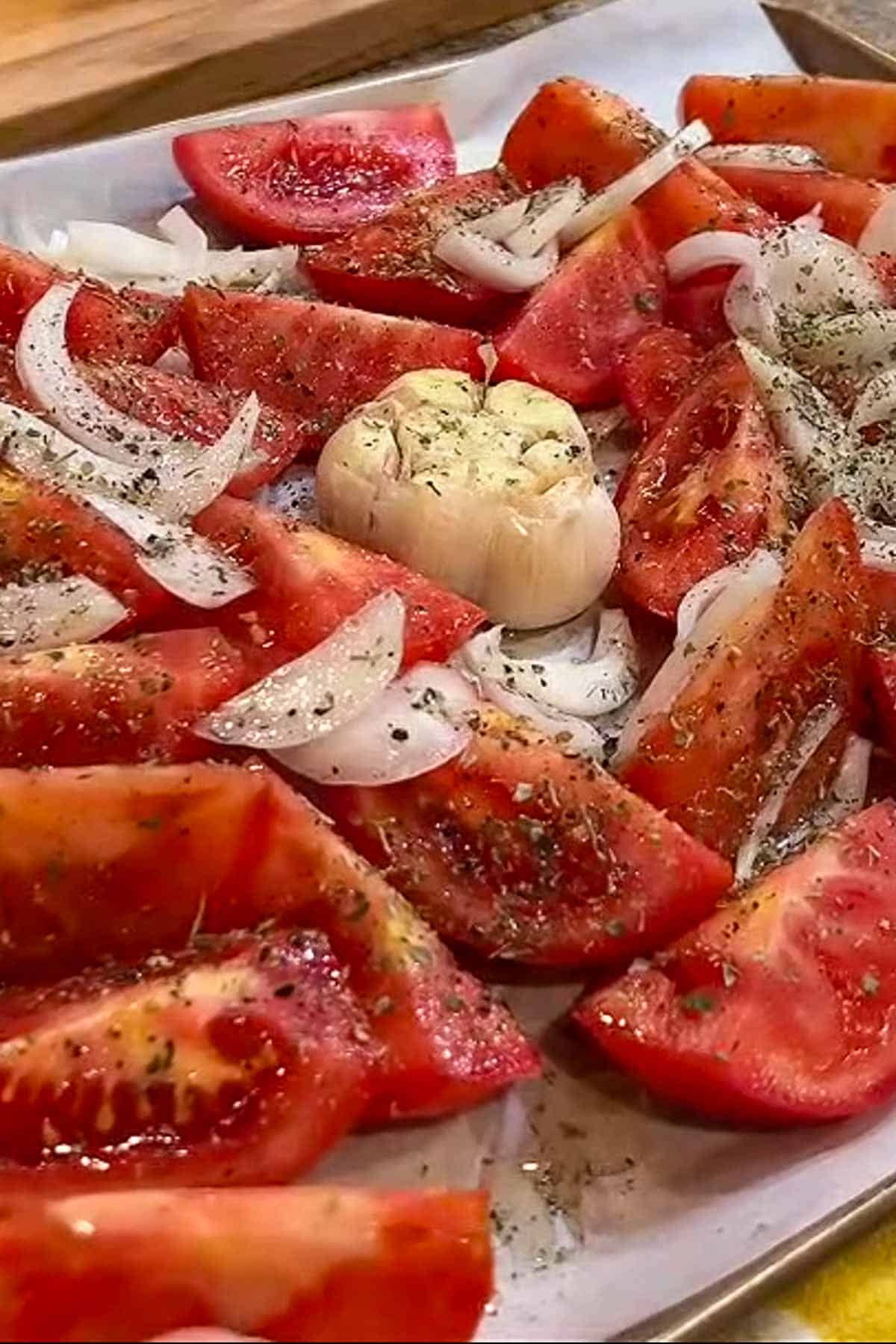 Chunks of tomatoes, sliced onions and a head of garlic on a sheet pan.