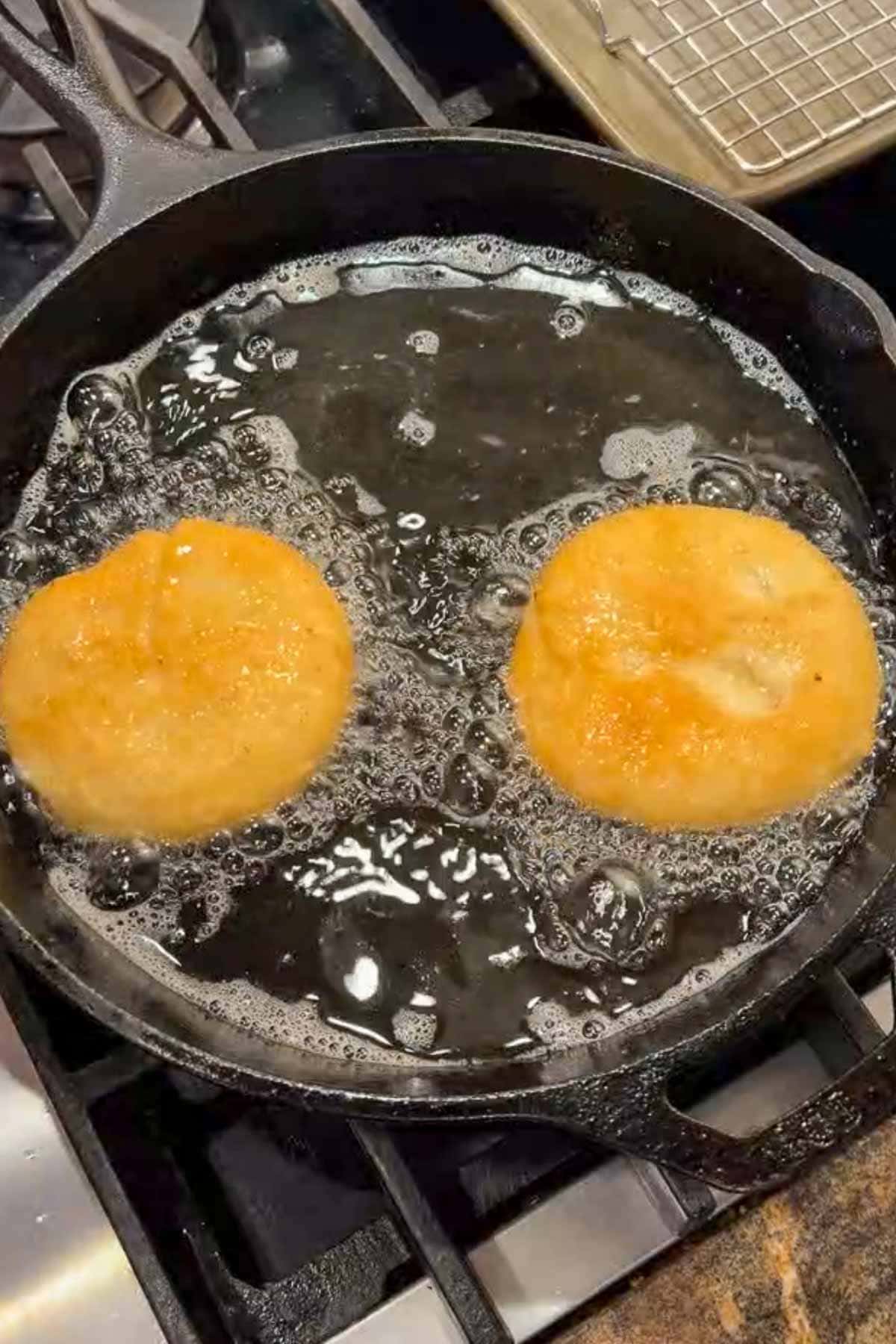 Two pizza fritta dough discs being fried in oil.
