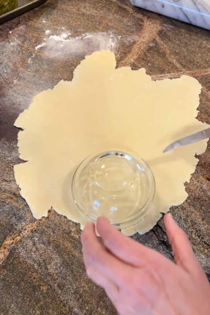 A glass bowl is set on dough that has been rolled out on a granite counter.