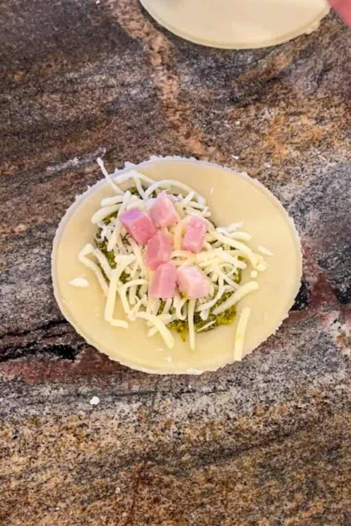 A round of dough topped with pesto, shredded cheese and ham. 