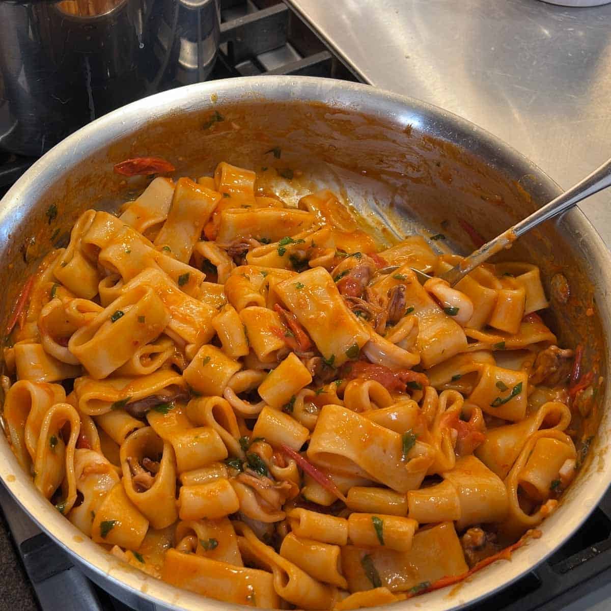 Calamarata pasta in a tomato and calamari sauce in a saute pan.