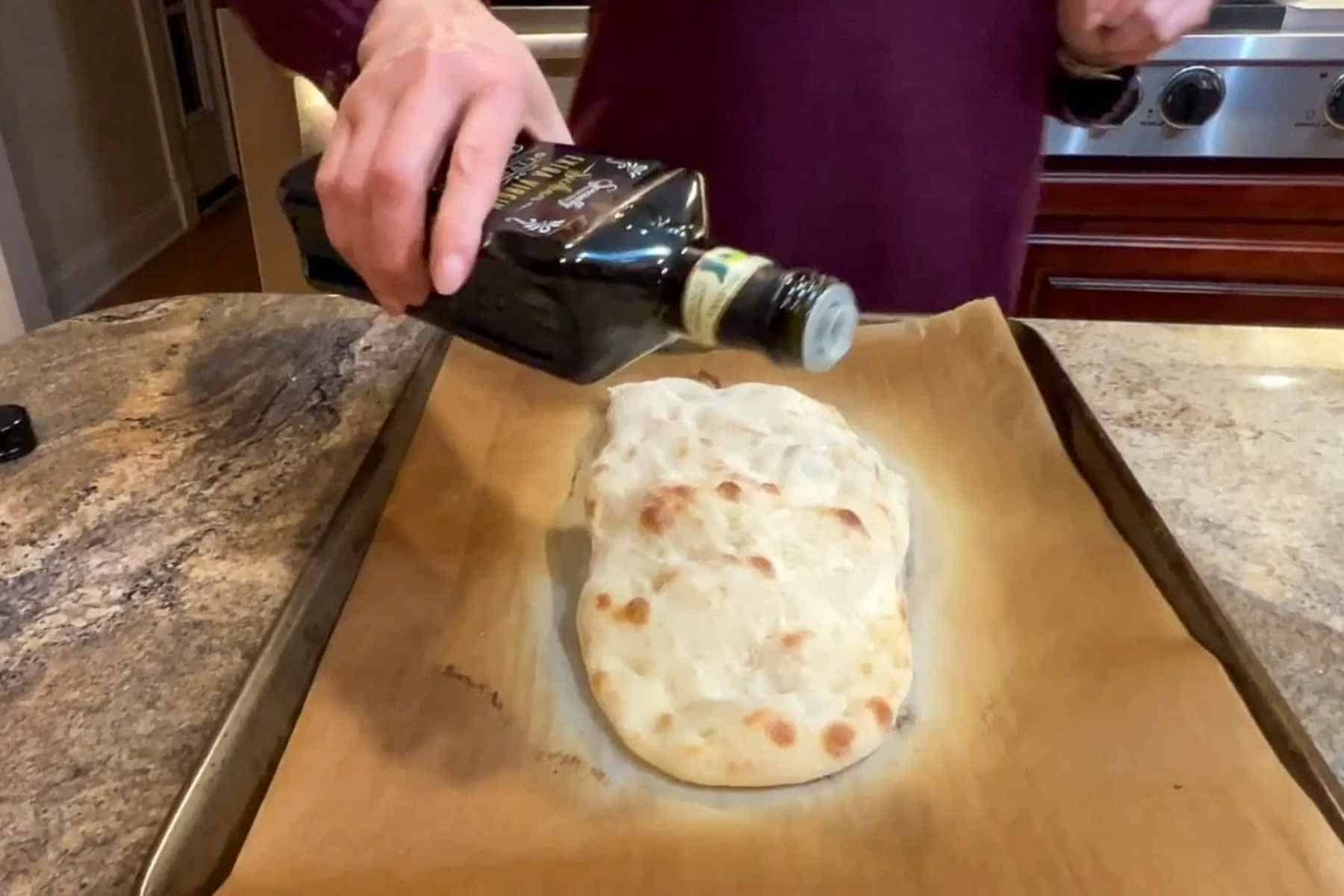 Pouring oil on a par baked pinsa romana.  