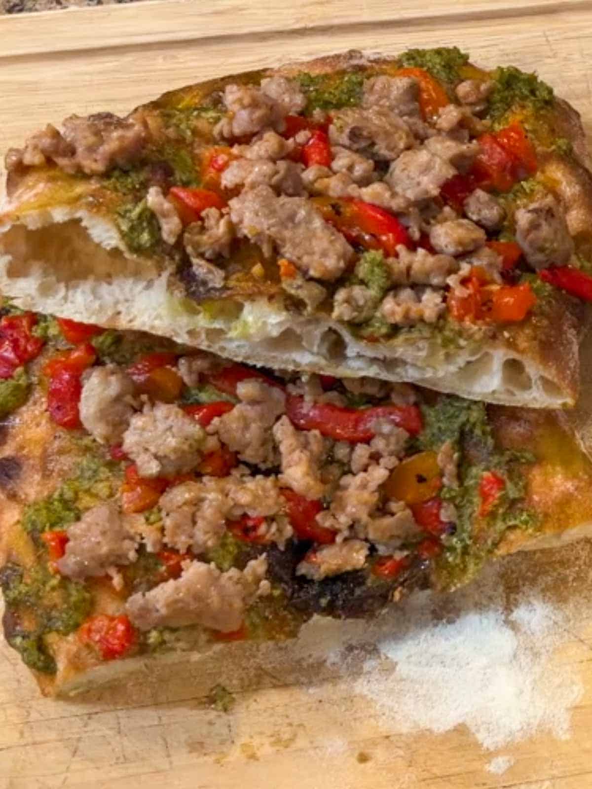 A pinsa Romana topped with sausage, pesto and roasted red peppers, cut in half to show the large bubbles in the dough.