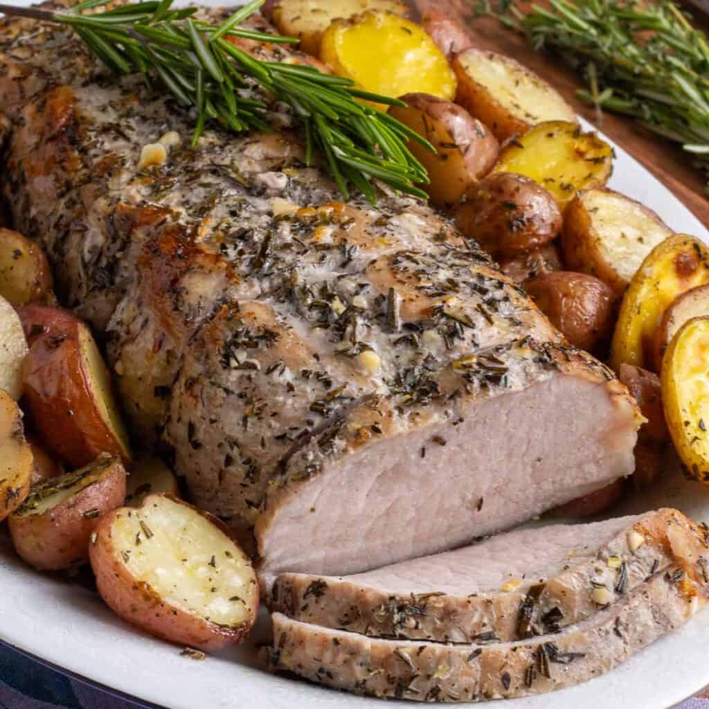 Arista al forno con patate on a platter with a sprig of rosemary on top.